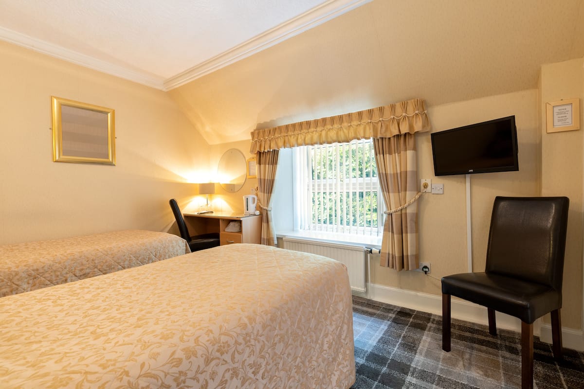 A hotel room with two beds, a desk with a lamp, a chair, a television, and a window with curtains.