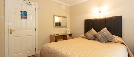 A hotel room with a bed, a bedside table, a mirror, a door with a sign, and a light fixture above the bed.