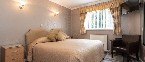A bedroom with a bed, bedside table, lamp, chair, and a window with curtains.