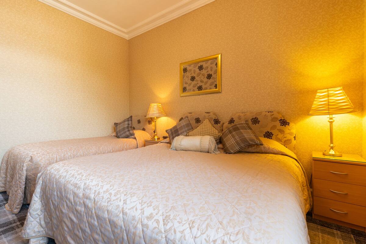 A double bed with a floral bedspread, two bedside tables with lamps, and a framed floral artwork on the wall.