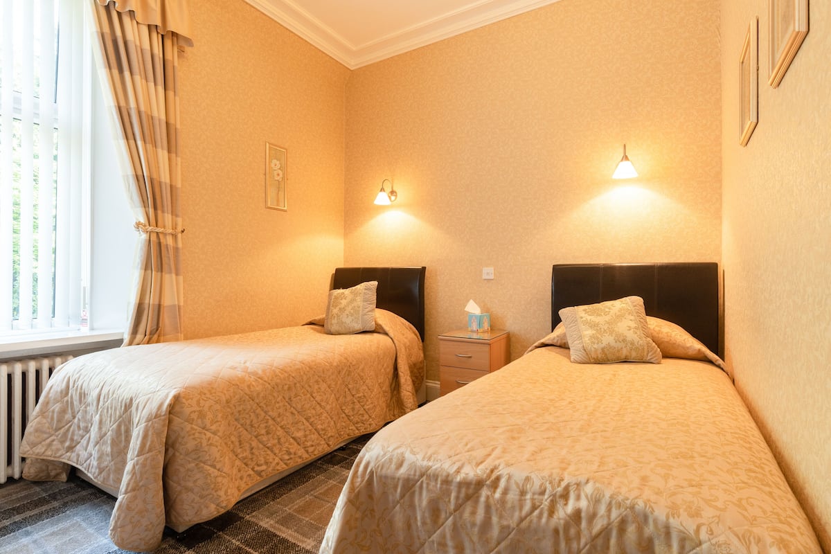 A hotel room with two beds, a window with curtains, bedside lamps, and a radiator.
