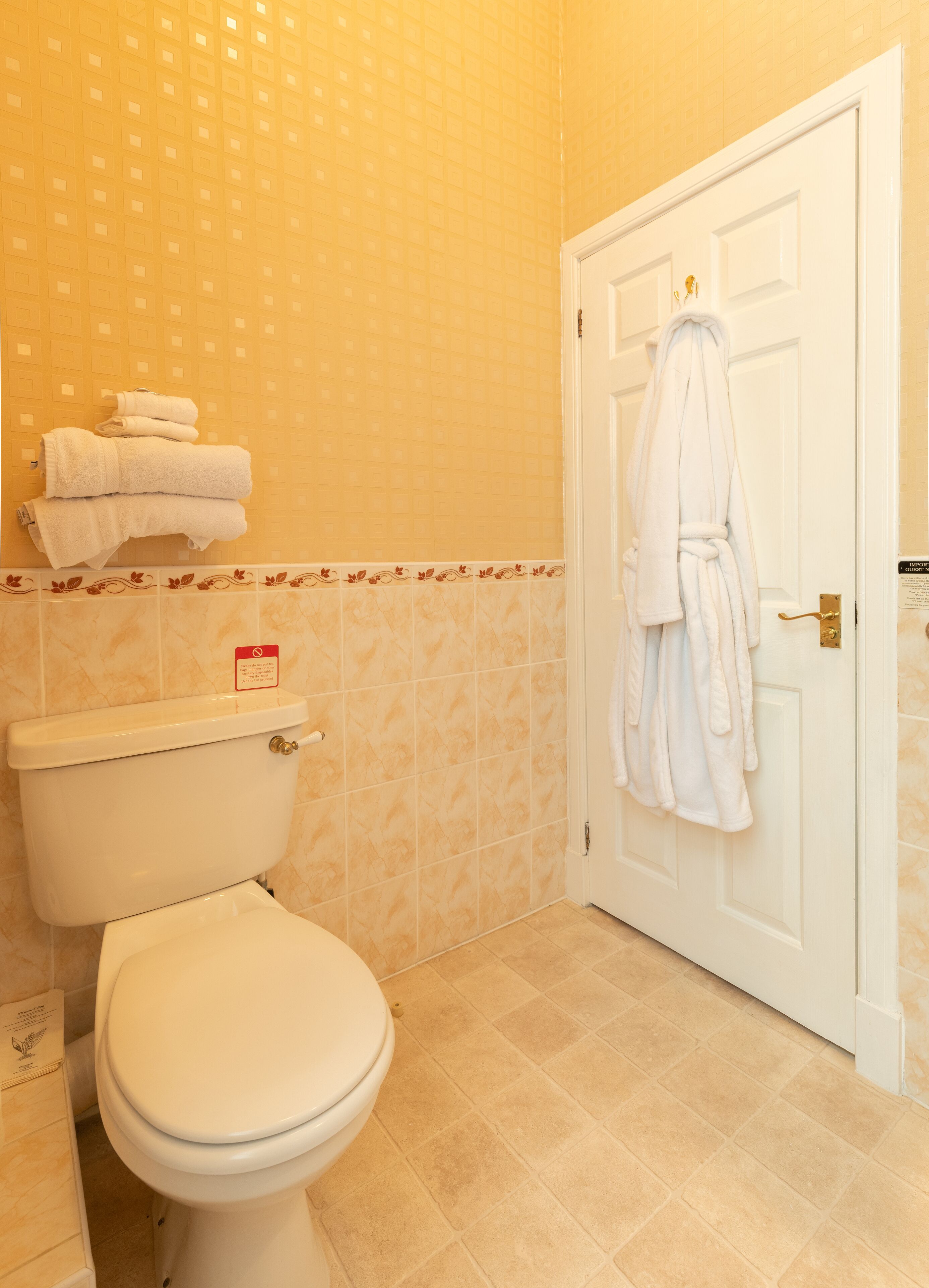 A bathroom with a toilet, a towel rack with folded towels, and a door with a robe hanging on it.