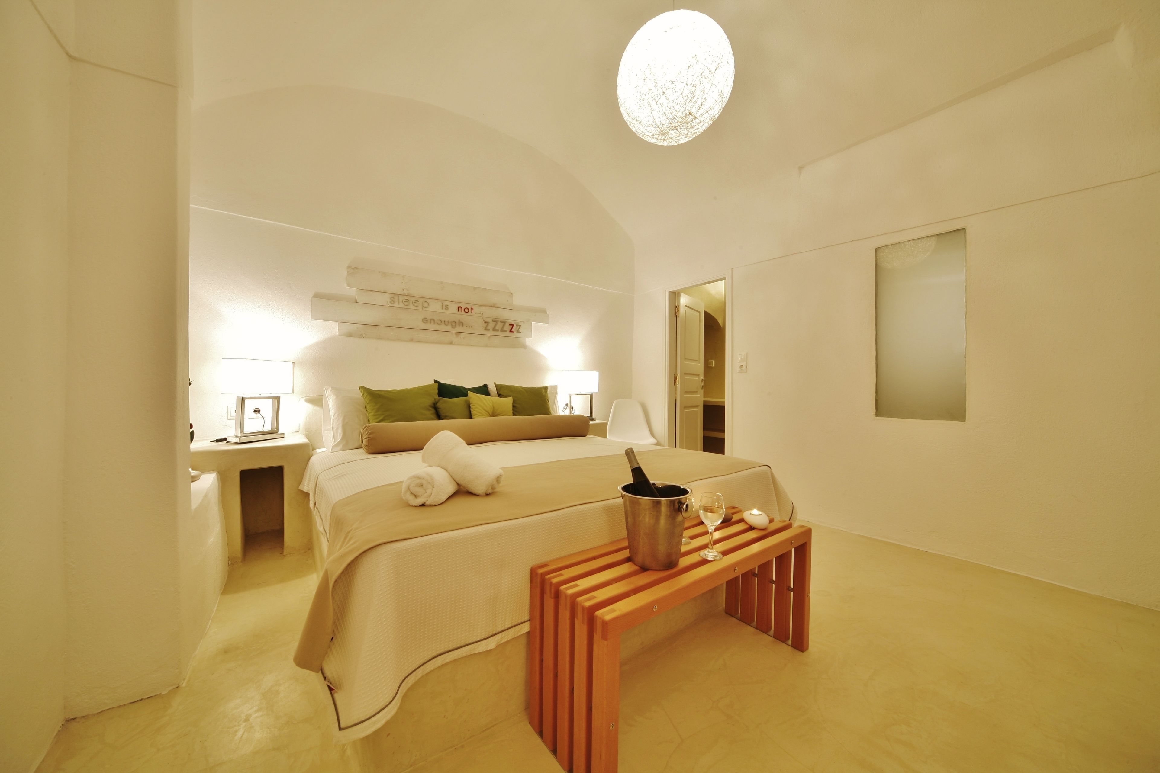 Ein modernes Schlafzimmer mit Bett, Nachttisch und einer kleinen Holzbank mit Flasche und Glas.