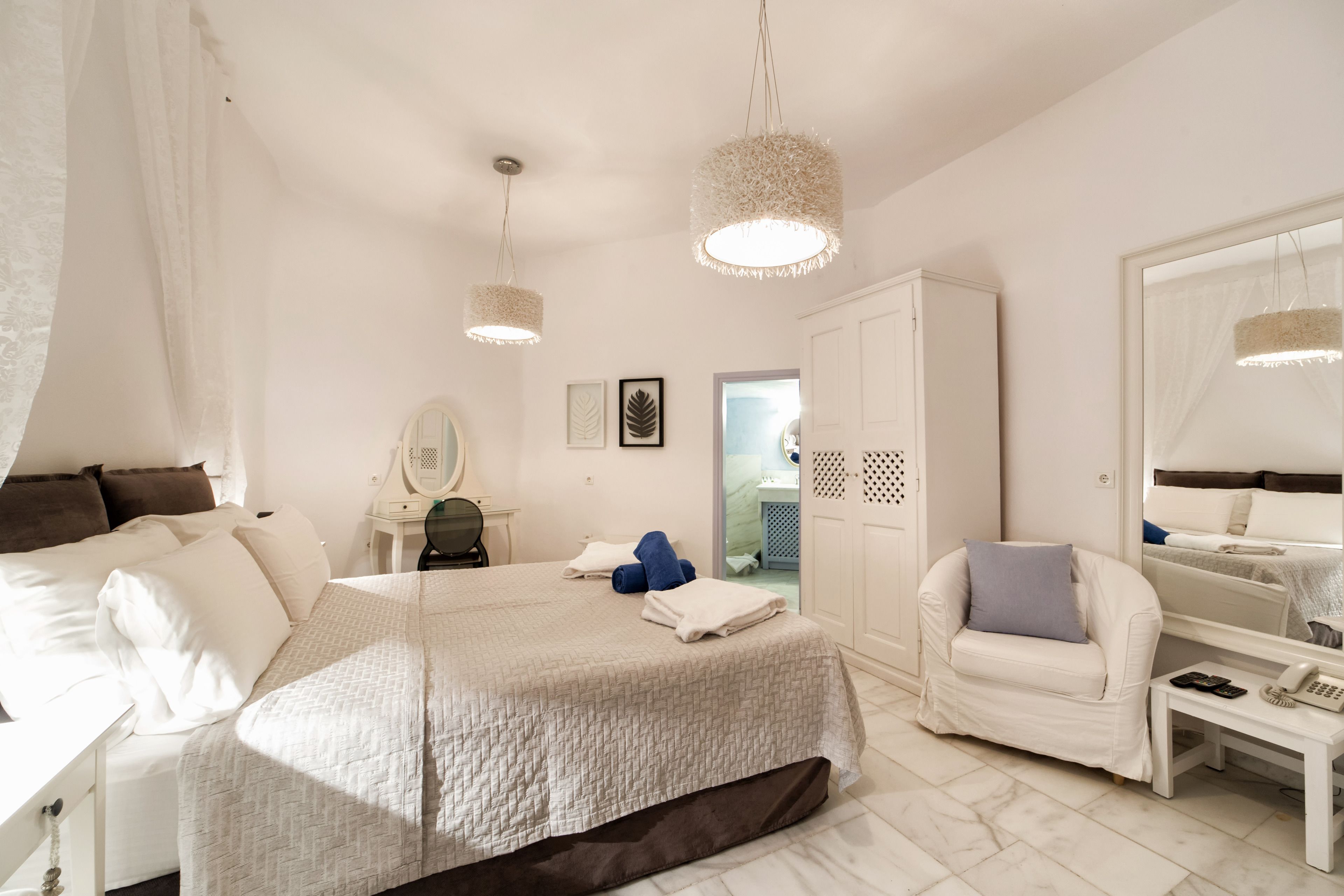 Et hotelværelse med en stor seng, et siddeområde med en stol, et skrivebord og en garderobe.