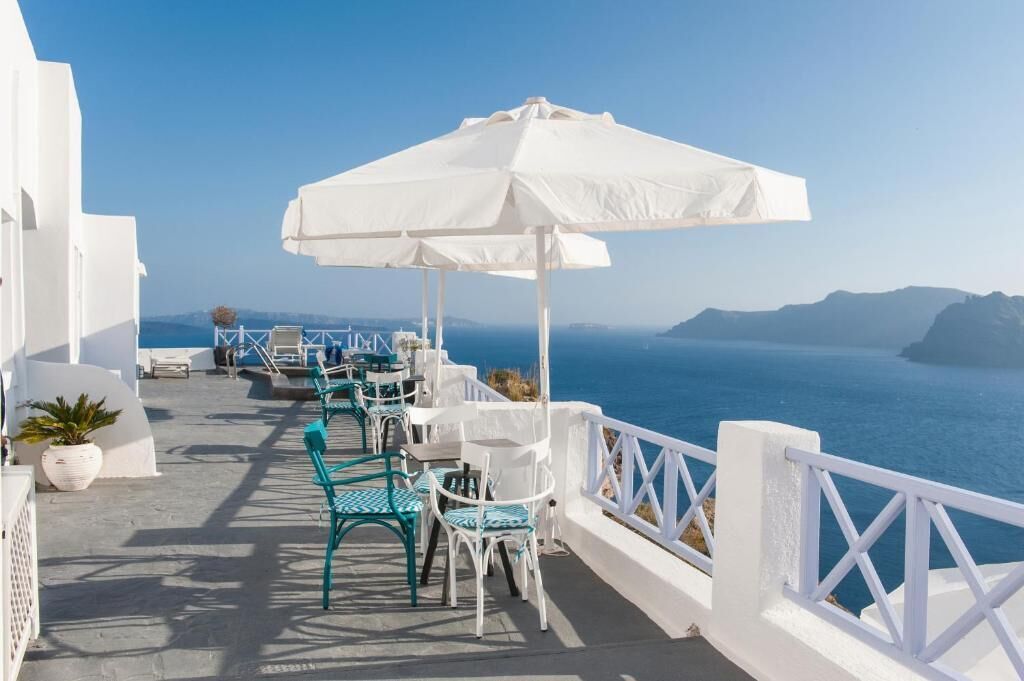 A seaside terrace with white railings, a white umbrella, and green and white chairs.