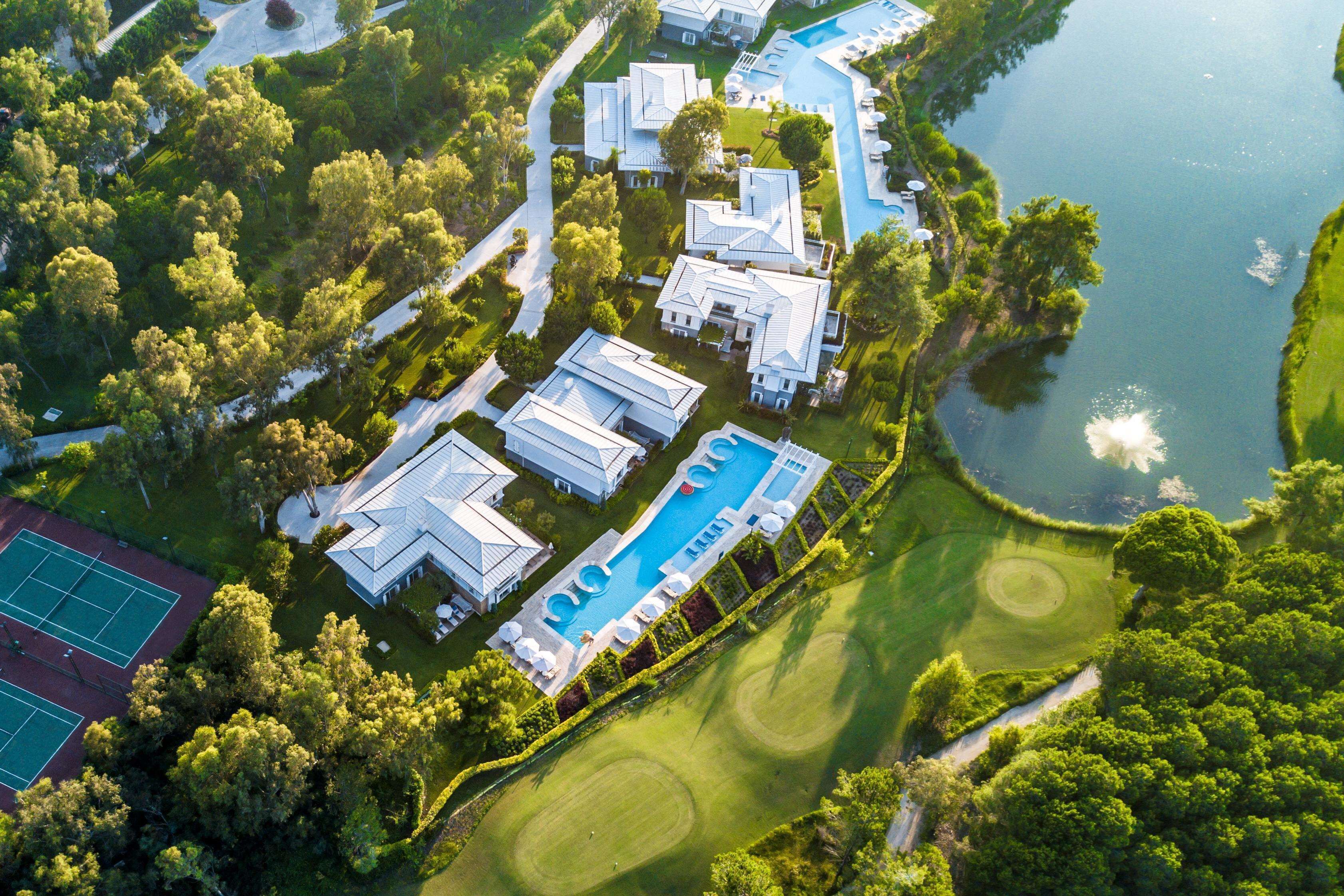 An aerial view of a resort with multiple buildings, a swimming pool, tennis courts, and a golf course.