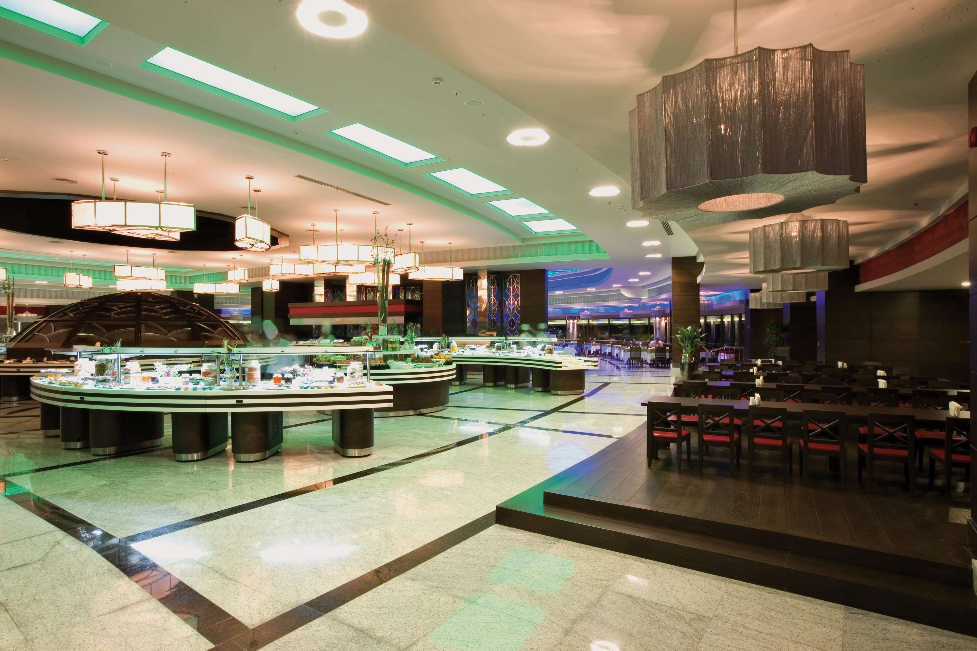 A modern hotel lobby with a central round bar, multiple seating areas, and a high ceiling with recessed lighting.