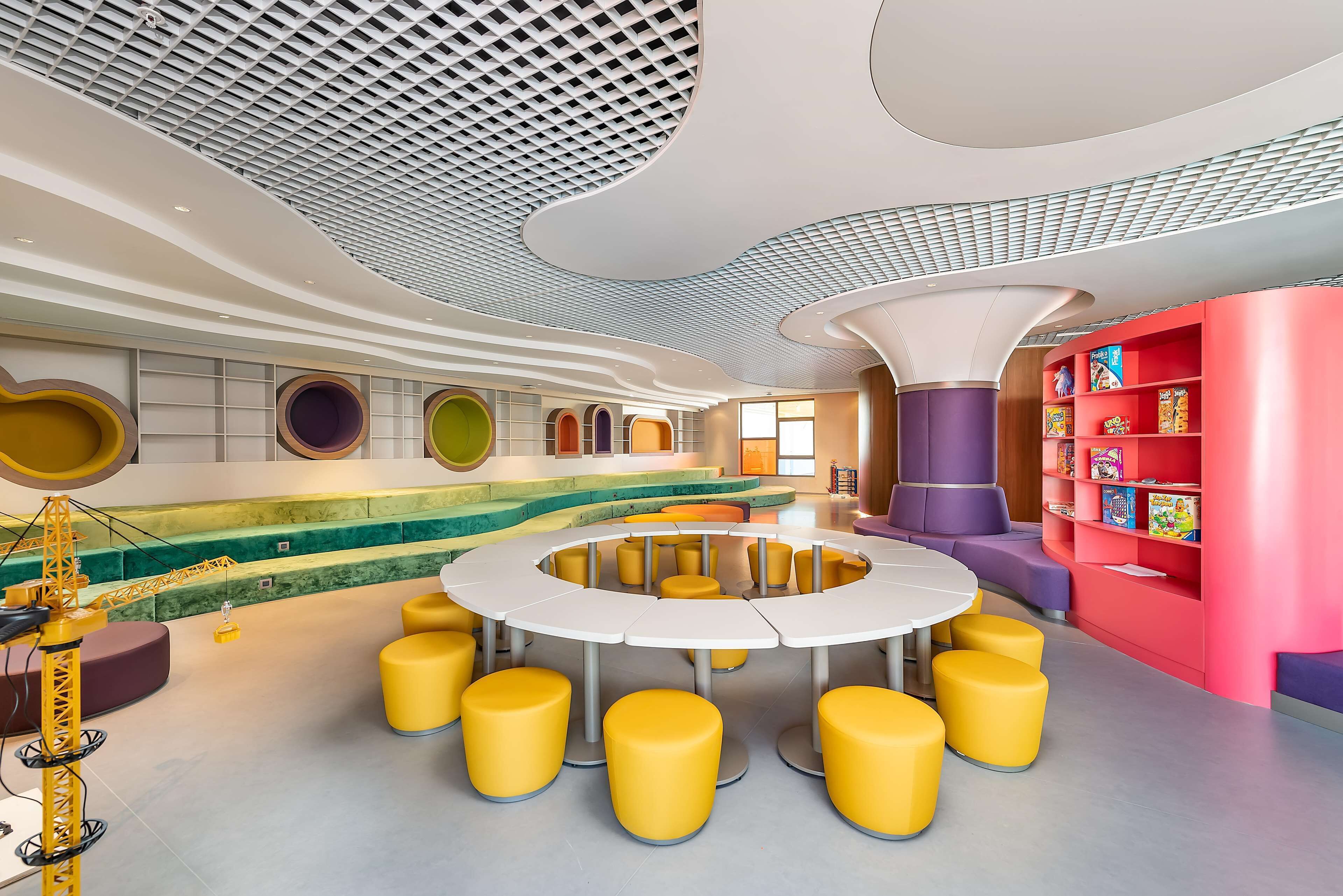 Spazio interno moderno con una zona salotto circolare, una libreria colorata e un design di soffitto originale.