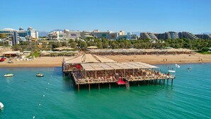 Un hotel frente al mar con un muelle que se adentra en el océano, con vistas a la playa y al paisaje urbano.
