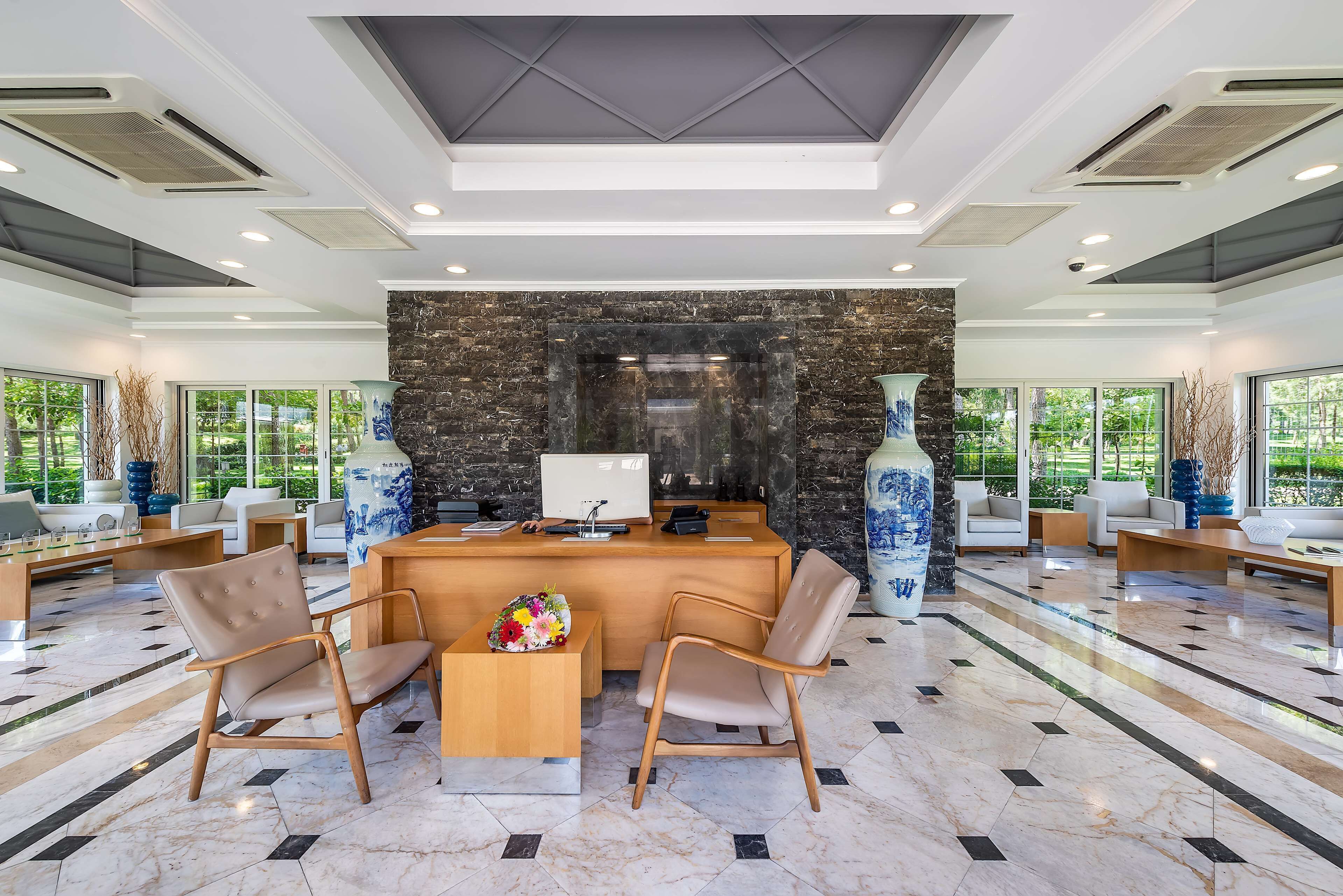 A modern reception area with a stone wall, a reception desk, two beige chairs, and a large vase.