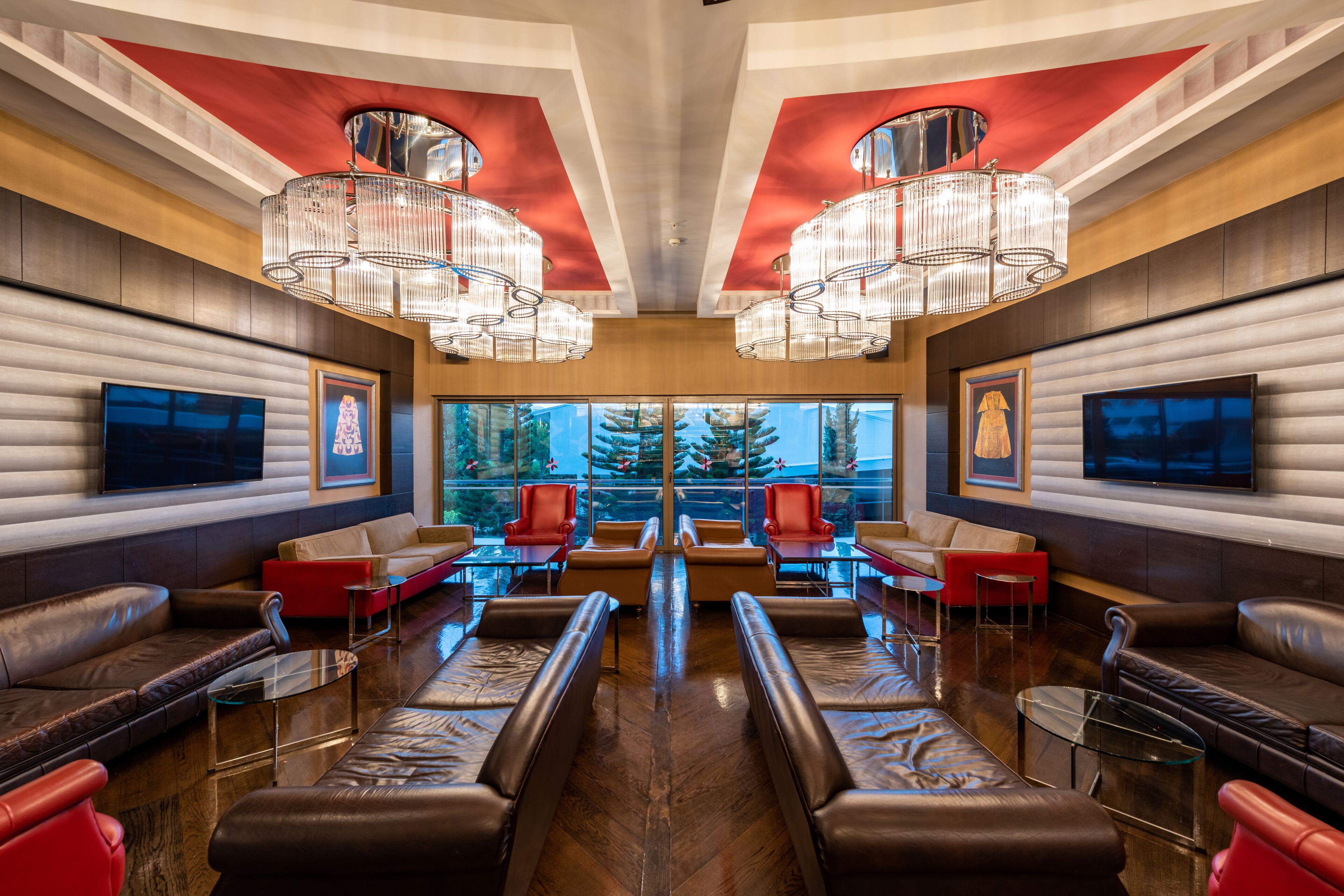 Un salón moderno con sofás de cuero, sillas rojas y un amplio ventanal con vistas a un árbol.