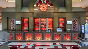 Un vestíbulo con un reloj grande, una zona de bar con iluminación roja y un mostrador de recepción.