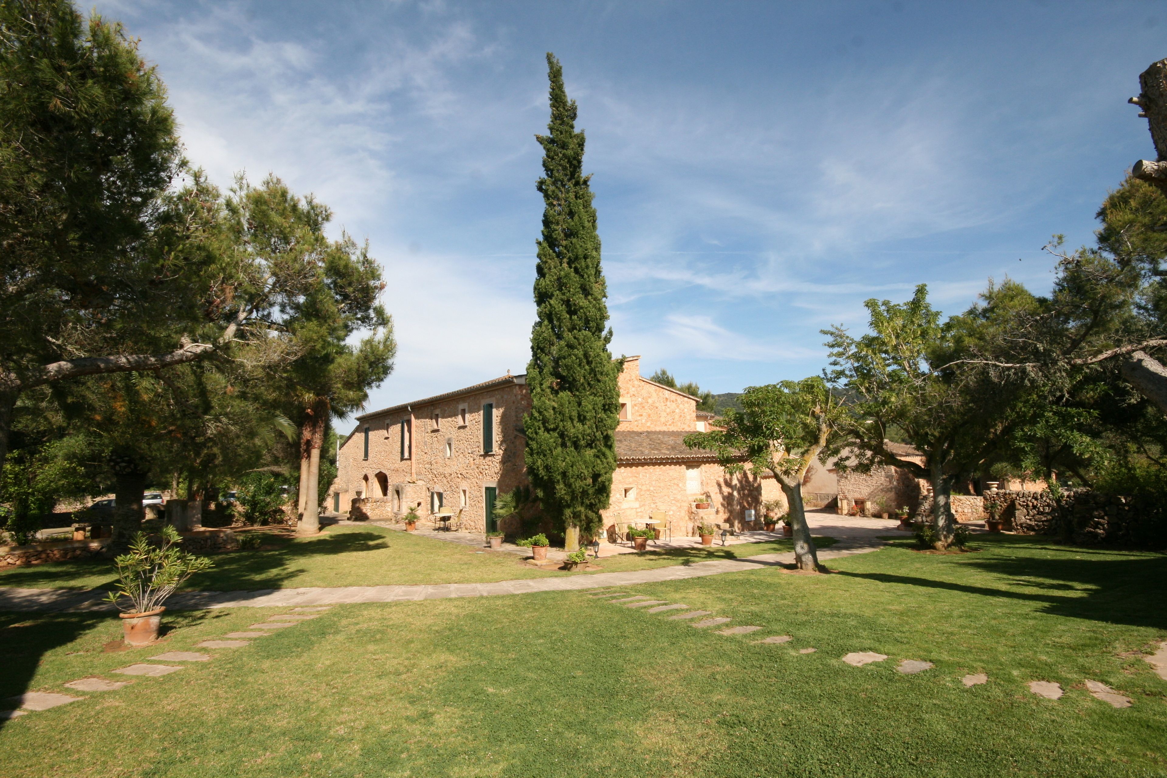A courtyard with a stone building, a tall cypress tree, and a well-maintained lawn.