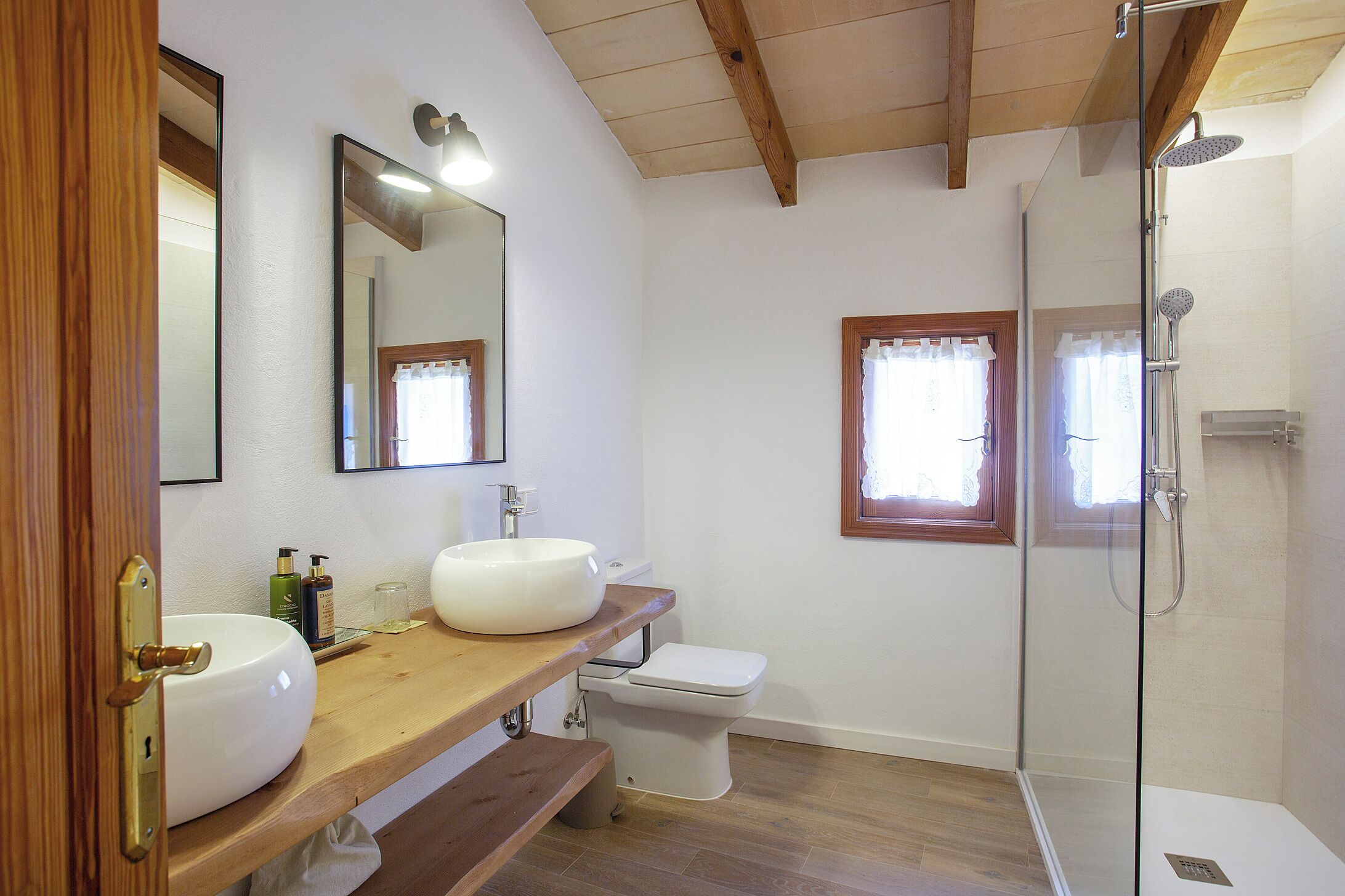 A bathroom with a wooden vanity, a white sink, a toilet, a shower, and a mirror.