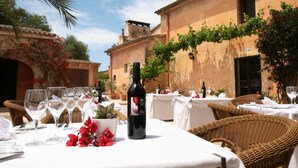 An outdoor dining area with wicker chairs and white tablecloths, a bottle of wine, and a potted plant. - Sa Galera Hotel Rural (Felanitx)
