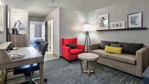 A hotel room with a desk, a red armchair, a sofa with a yellow pillow, a standing lamp, and framed pictures on the wall. - Country Inn & Suites by Radisson, Oklahoma City Airport, OK (Oklahoma City)
