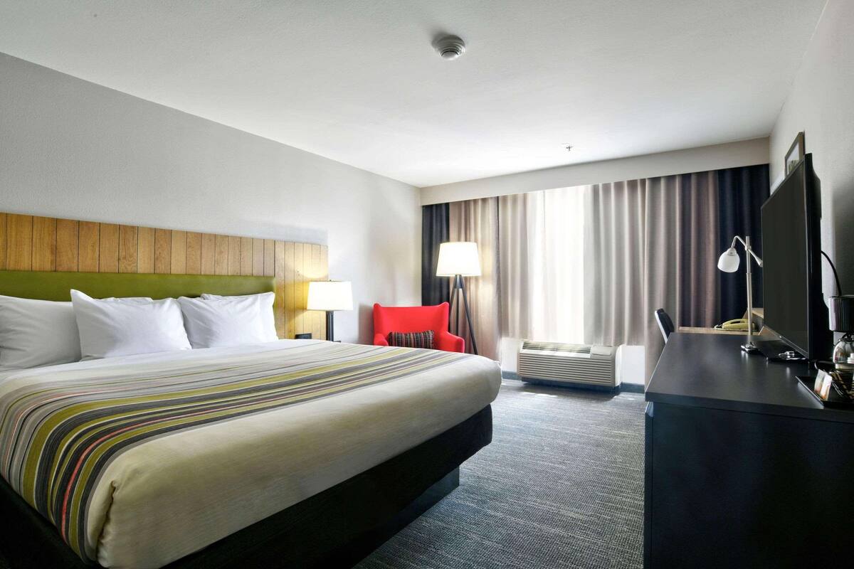 Una habitación de hotel con una cama grande, un escritorio con una computadora, una silla roja y un televisor.