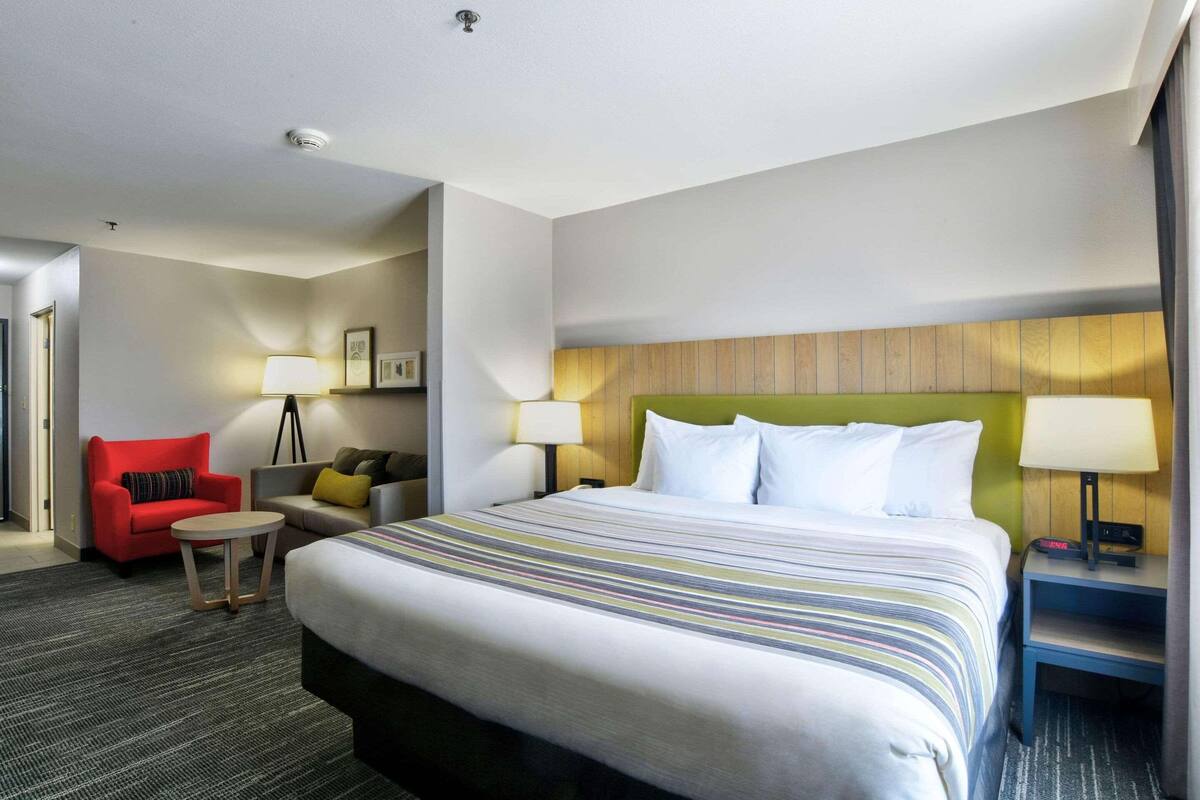 Una habitación de hotel con una cama grande, un sillón rojo, una mesita redonda y un sofá con cojines.