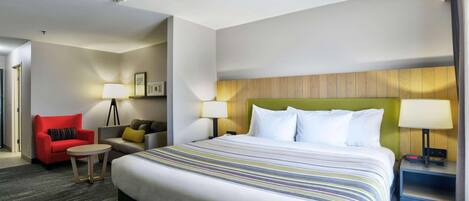 Una habitación de hotel con una cama grande, un sillón rojo, una mesita redonda y un sofá con cojines.