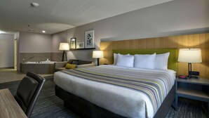 A hotel room with a large bed, a desk, a chair, a sofa, a bathtub, and a nightstand with a lamp. - Country Inn & Suites by Radisson, Oklahoma City Airport, OK (Oklahoma City)