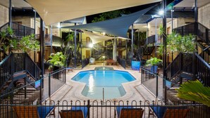 Una piscina con un deck circundante, bancos y plantas en macetas.