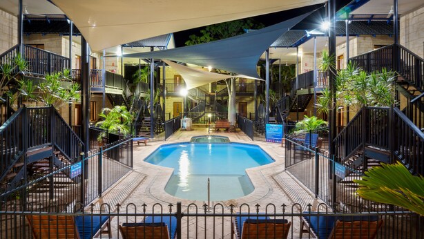 Une piscine entourée d’une terrasse, de bancs et de plantes en pot.
