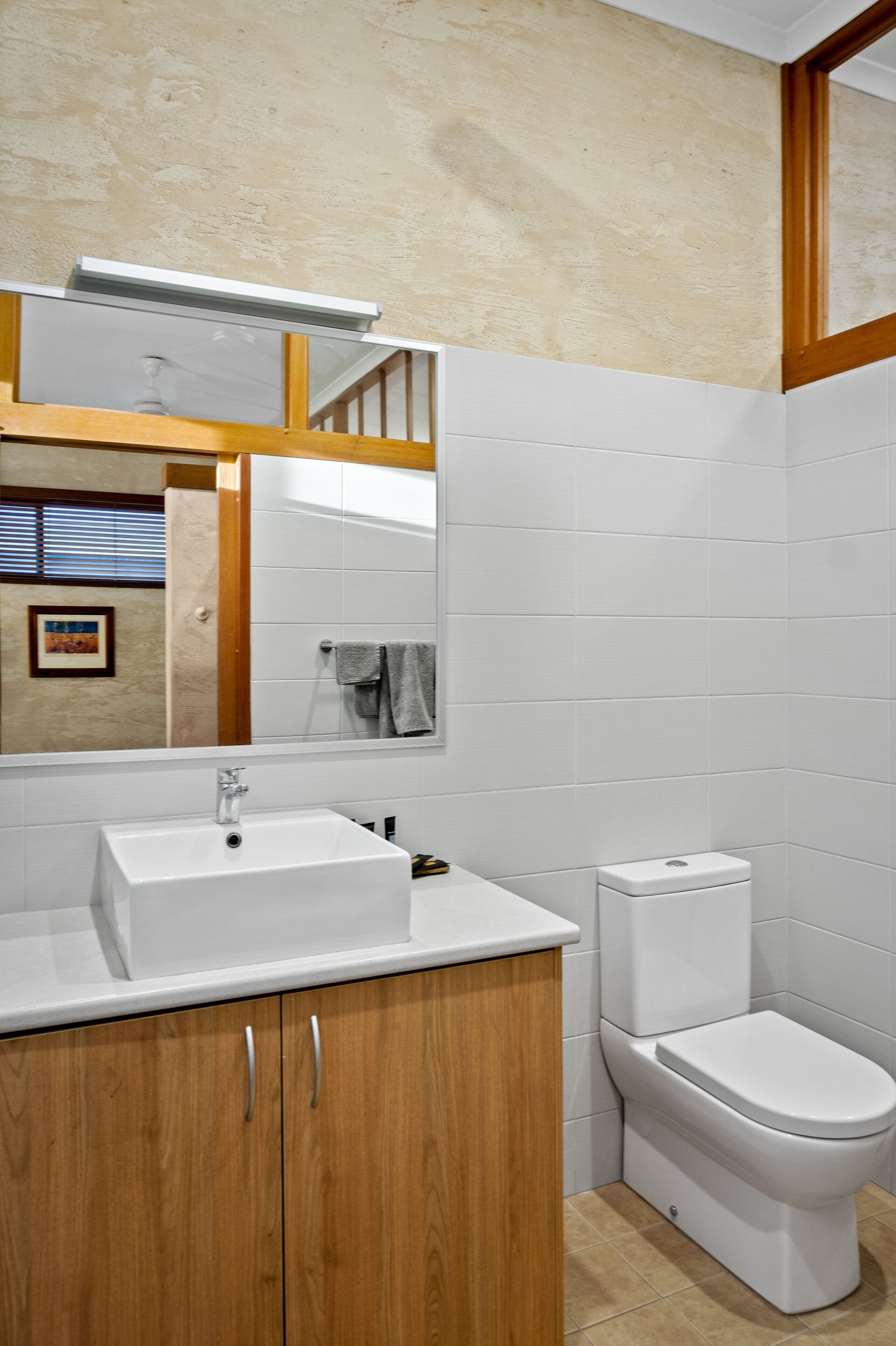 Un baño con un lavabo blanco, armarios de madera, un inodoro y un espejo.