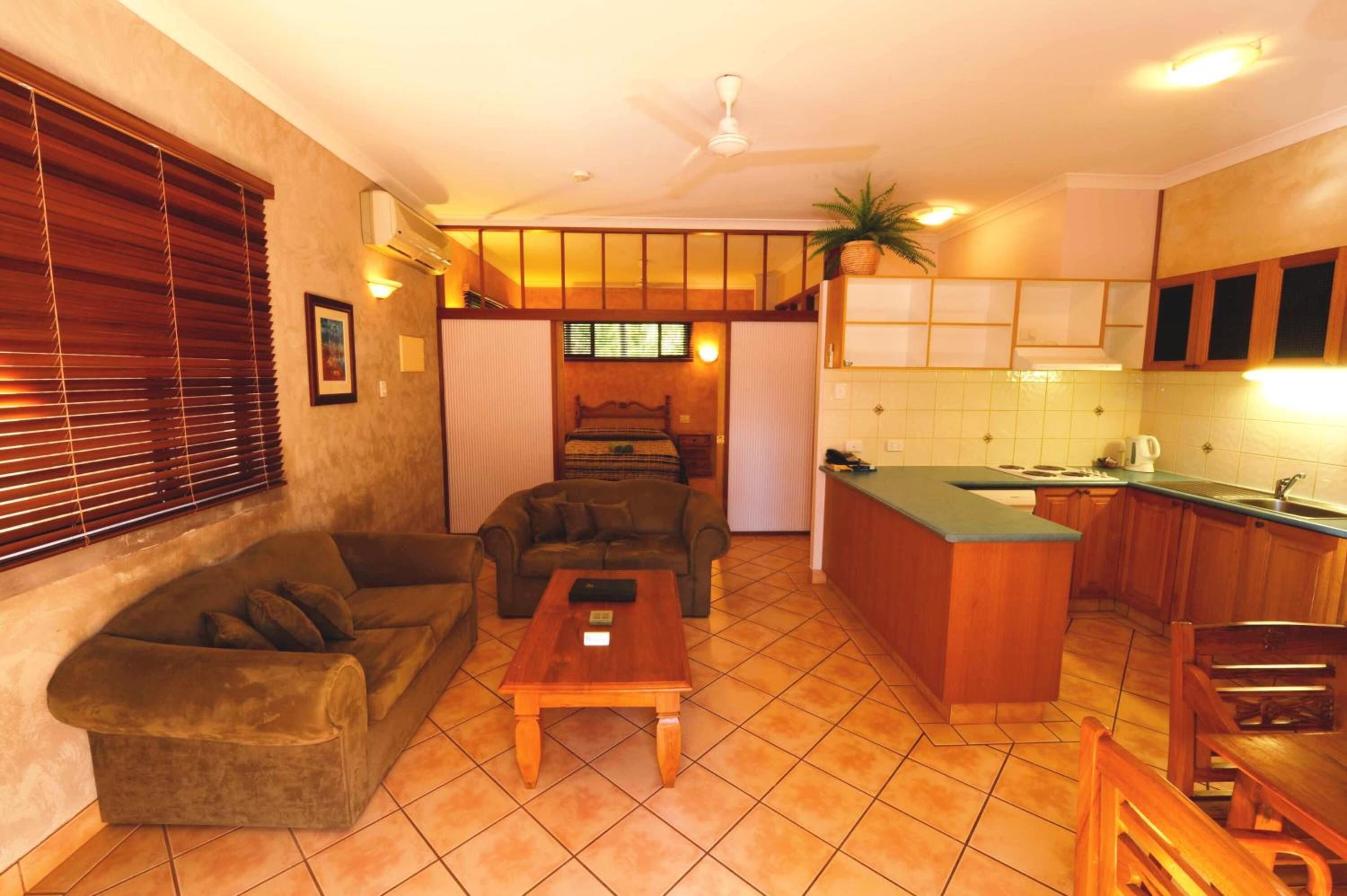 Un espace de vie compact comprenant un canapé, une petite table basse, une kitchenette avec un évier et un plan de travail, et un ventilateur de plafond.