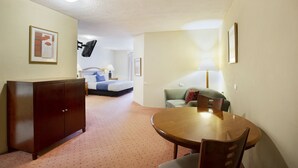A hotel room with a wooden dining table, a sofa, a bed, and a cabinet.