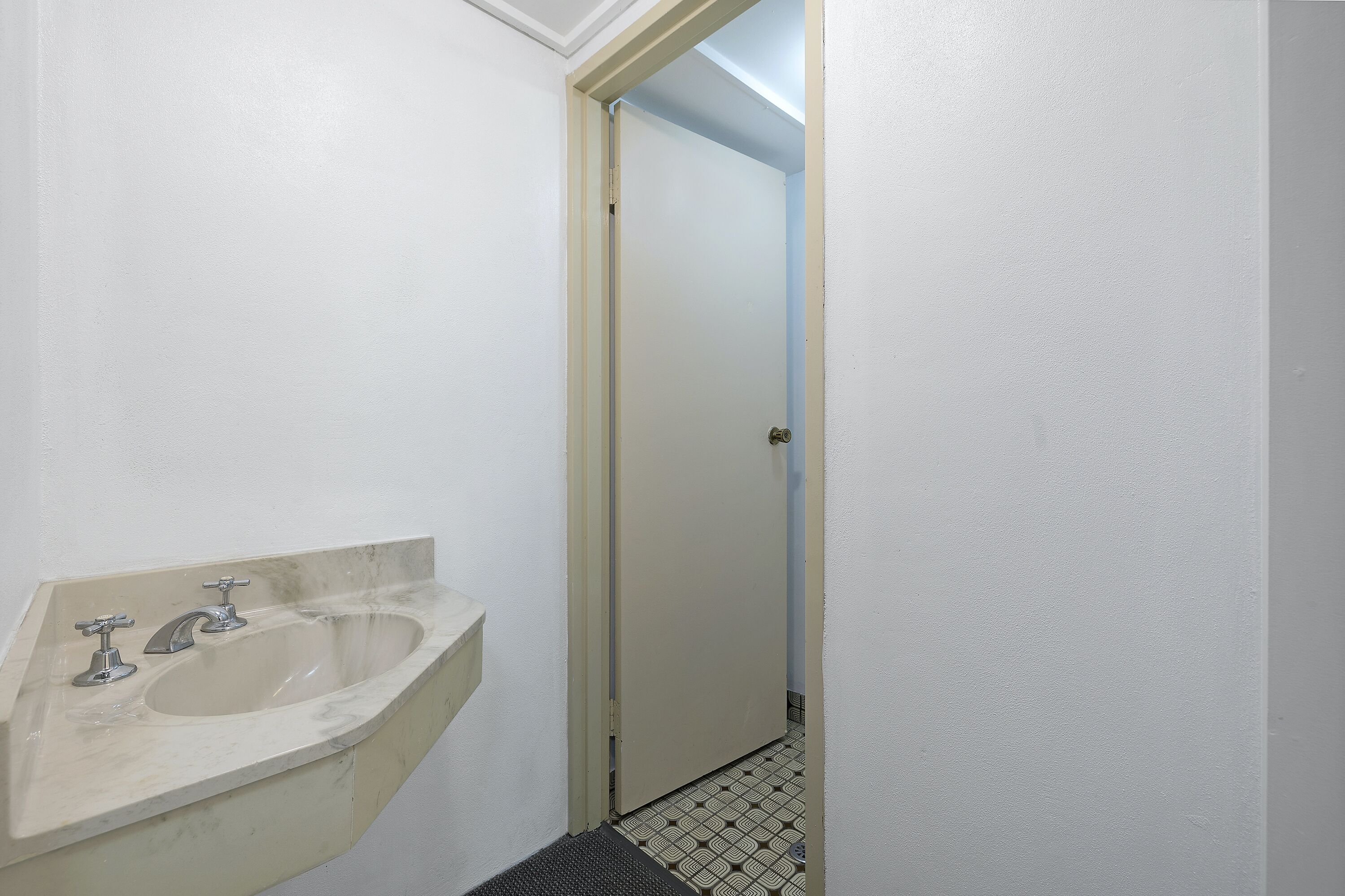 Un baño con un lavamanos, una puerta y un suelo estampado.
