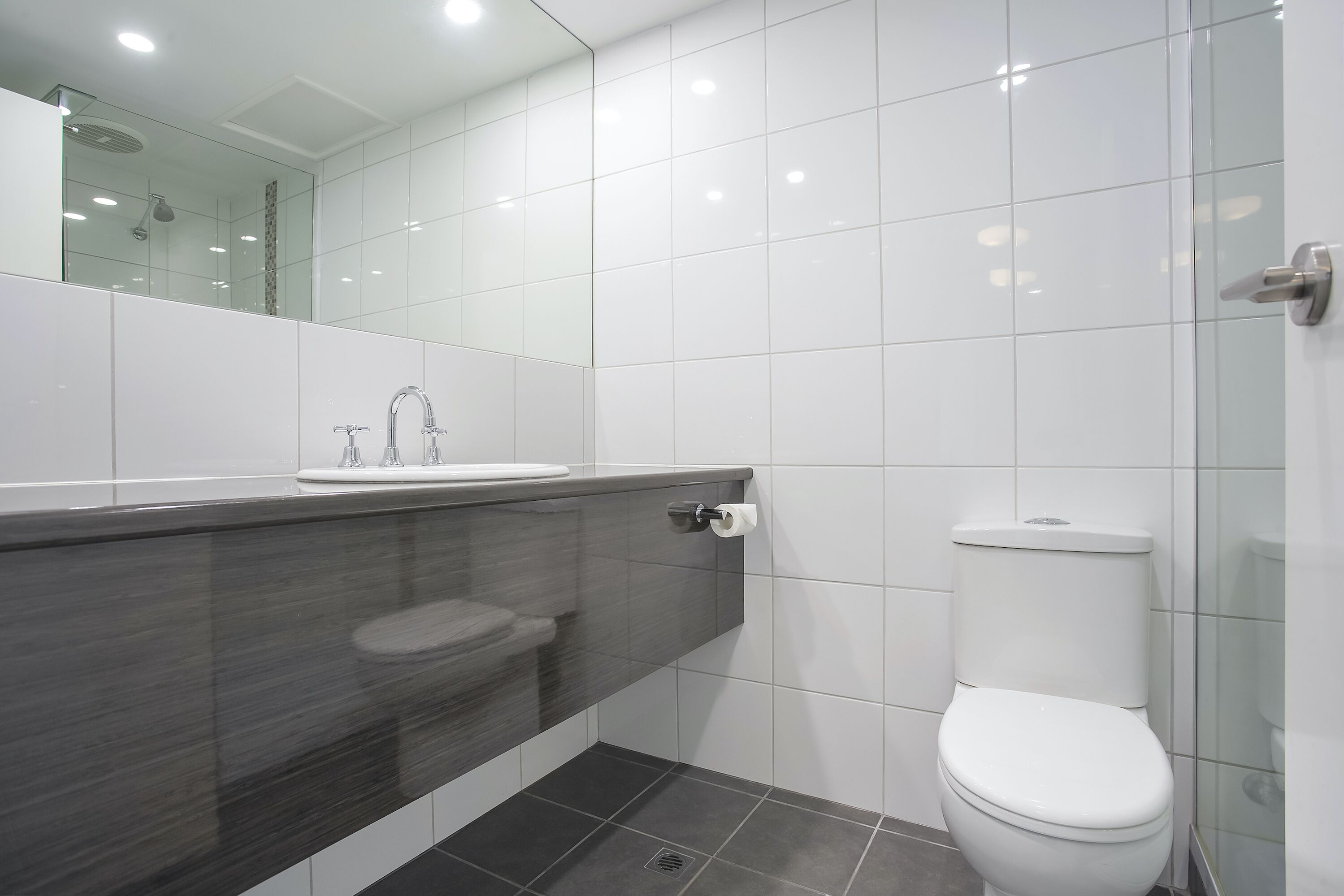 A modern bathroom with a glass shower enclosure, a white toilet, and a dark-toned vanity.