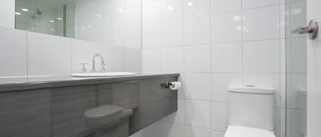 A modern bathroom with a glass shower enclosure, a white toilet, and a dark-toned vanity.
