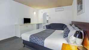 A neatly arranged hotel room with a bed, a desk, a television, and a mirror.
