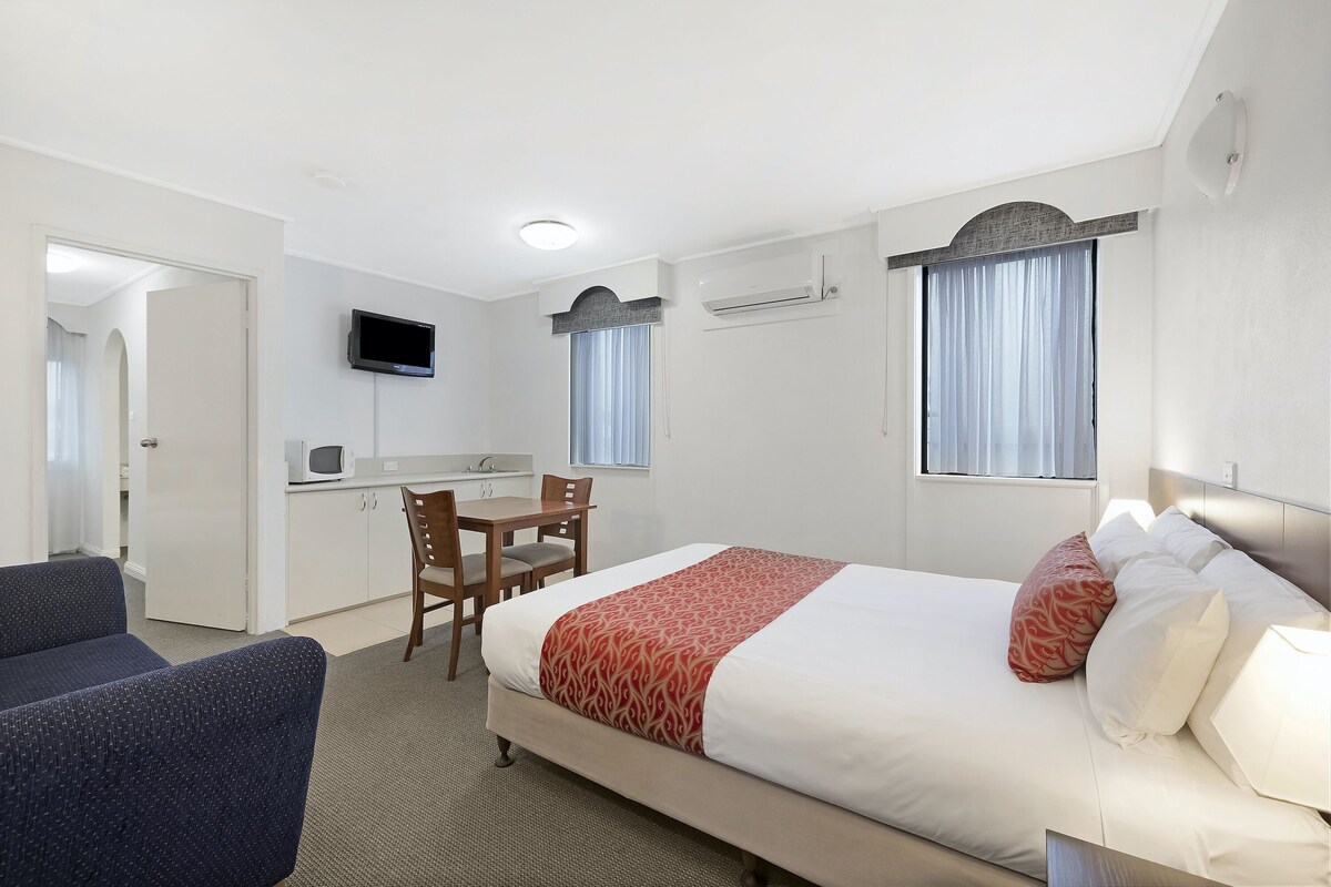 A hotel room with a bed, a desk, a chair, a TV, and a window.