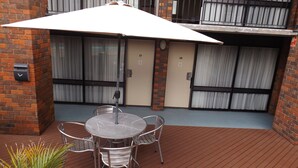 A patio with a round table and chairs, a white umbrella, and a brick wall.