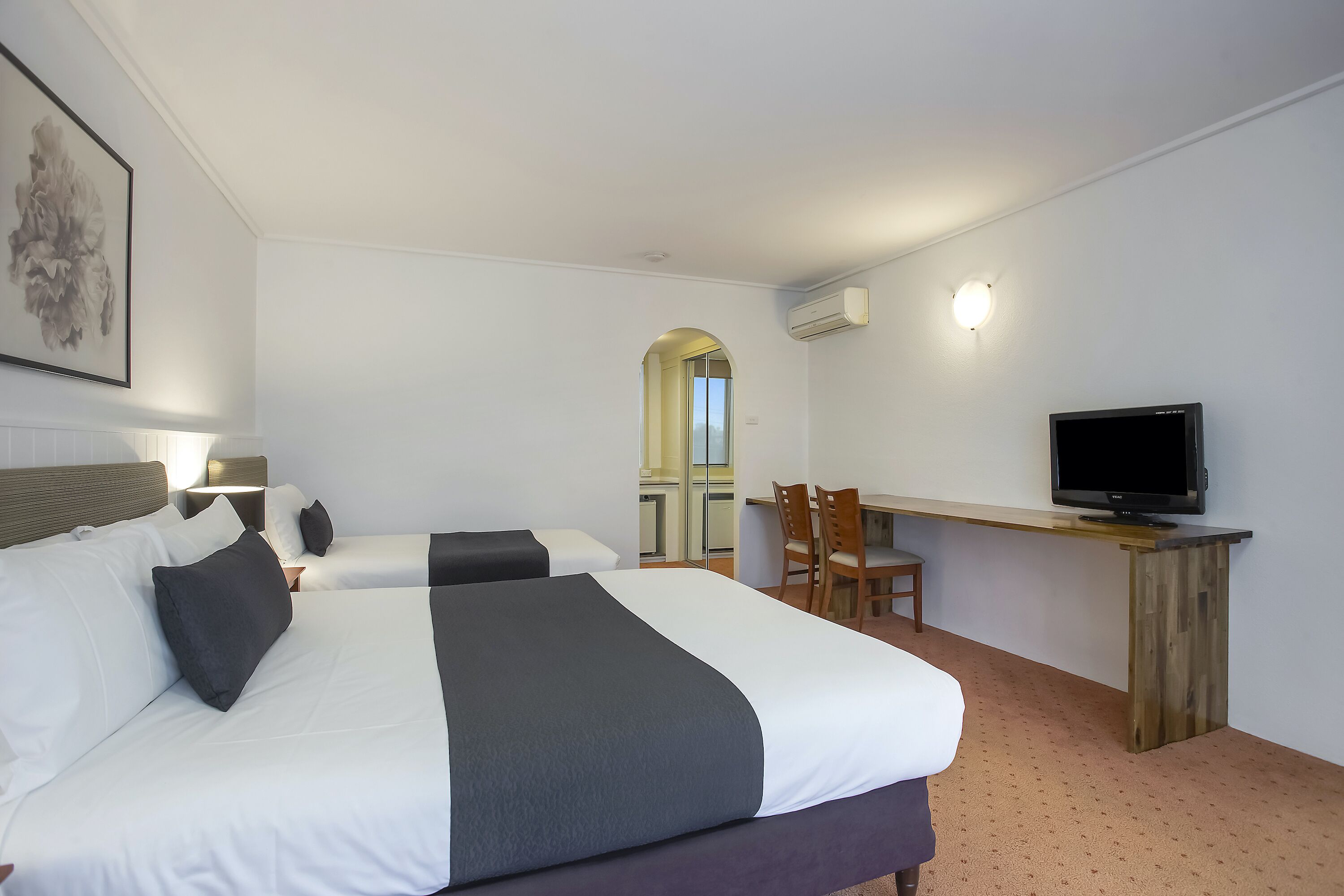 A hotel room with two beds, a desk with a TV, and a mirror.