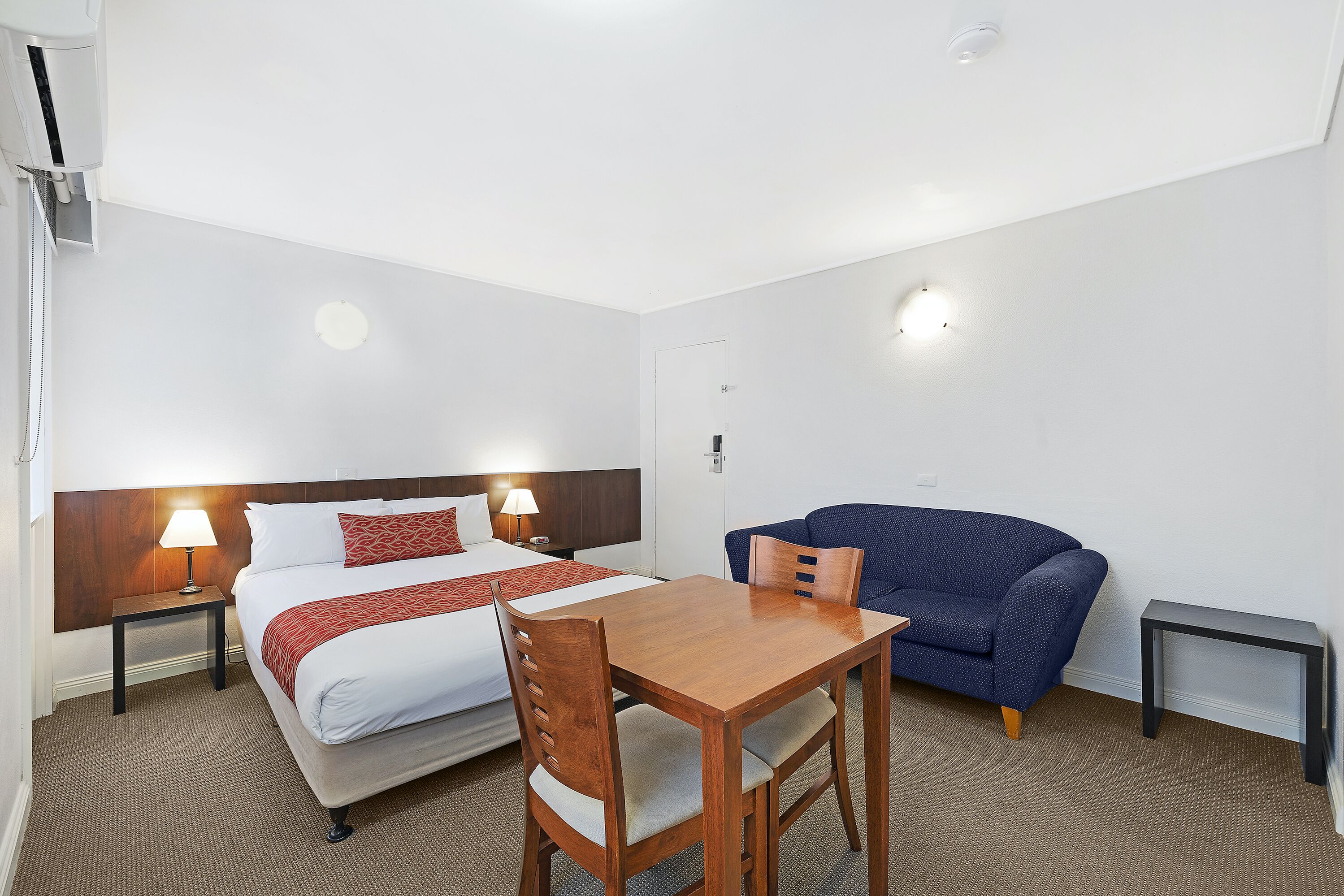 Une chambre d’hôtel avec un lit, une table en bois, un canapé bleu et deux lampes de chevet.