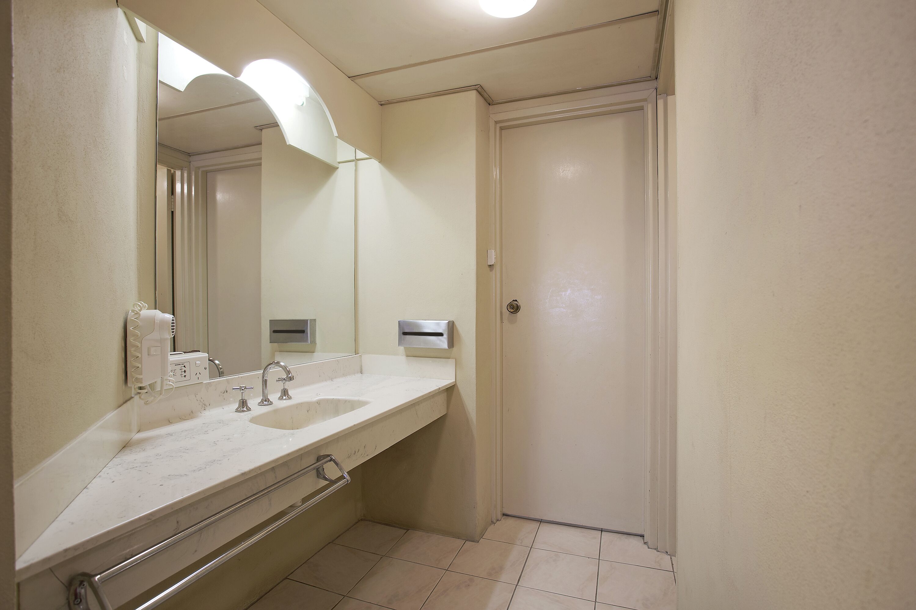 Un baño con un lavabo blanco, un espejo, un dispensador de toallas y una puerta.