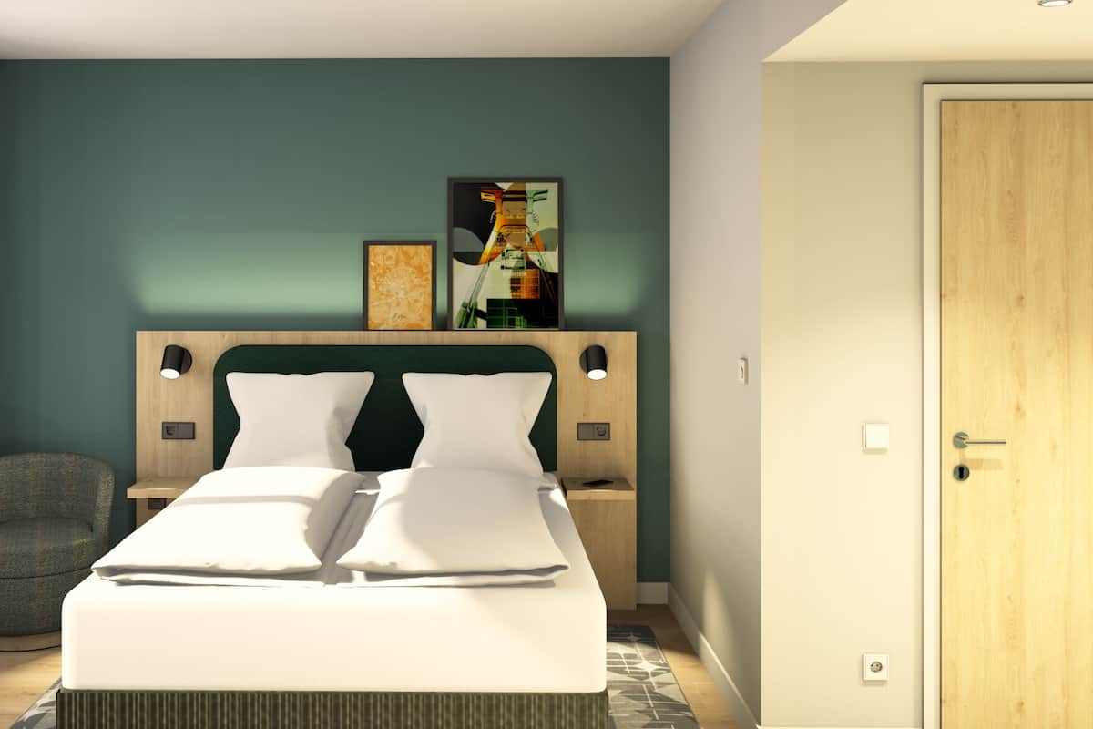 A modern hotel room with a large bed, two bedside tables, a chair, and artwork on the wall.
