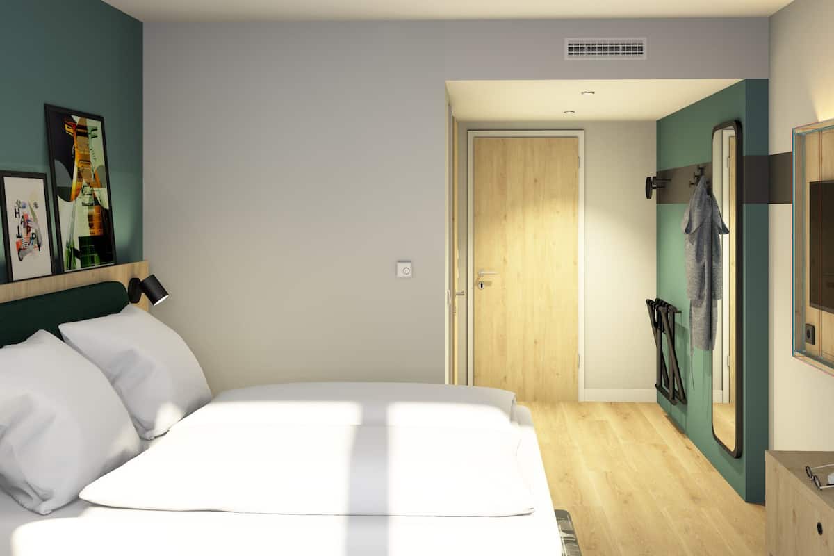 A modern bedroom with a bed, a TV, a desk, and a door leading to a bathroom.