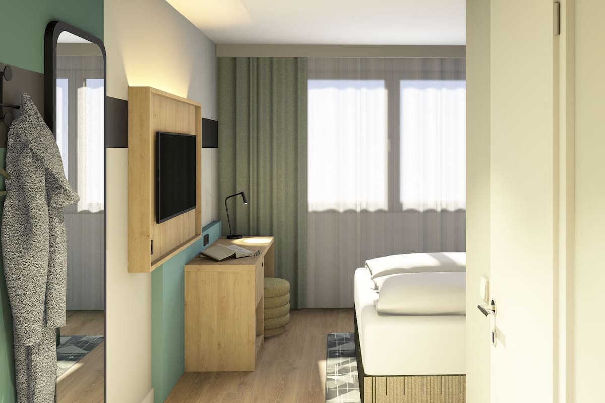 A modern hotel room with a bed, a desk with a TV, a mirror, and a window with curtains.