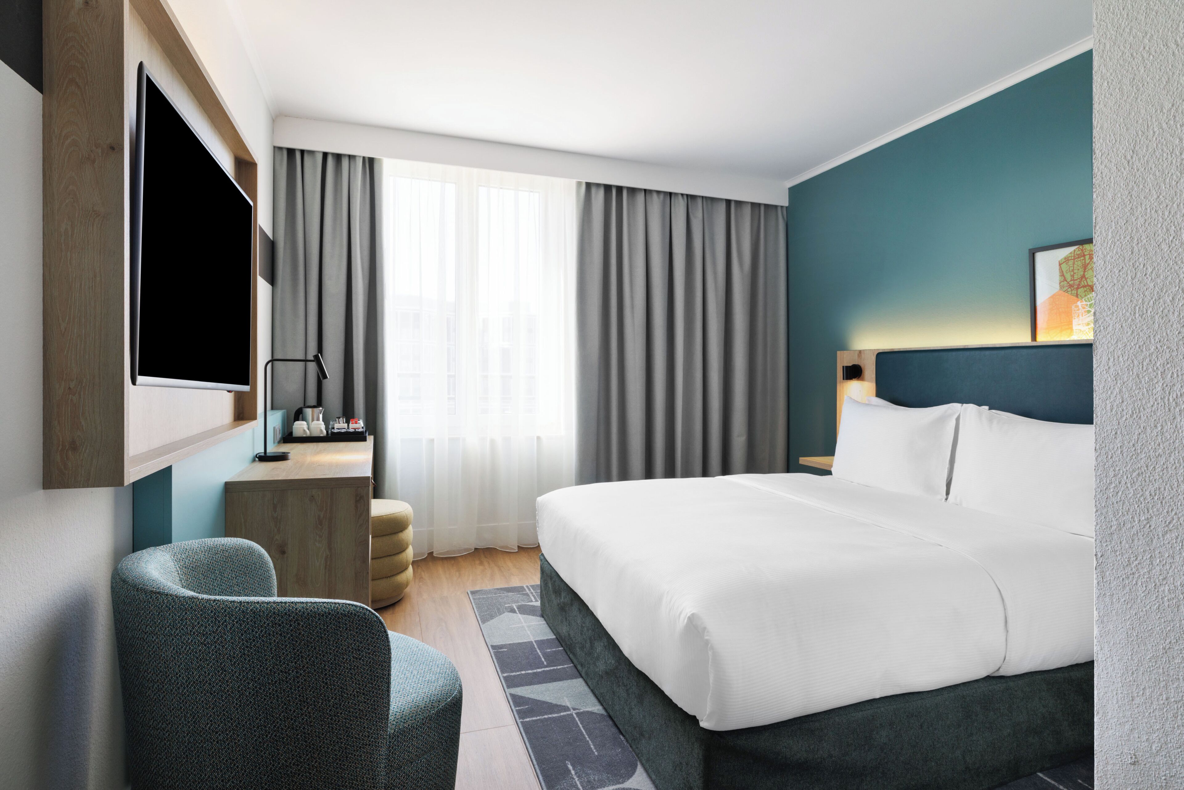A hotel room with a bed, a desk, a chair, a TV, and curtains.