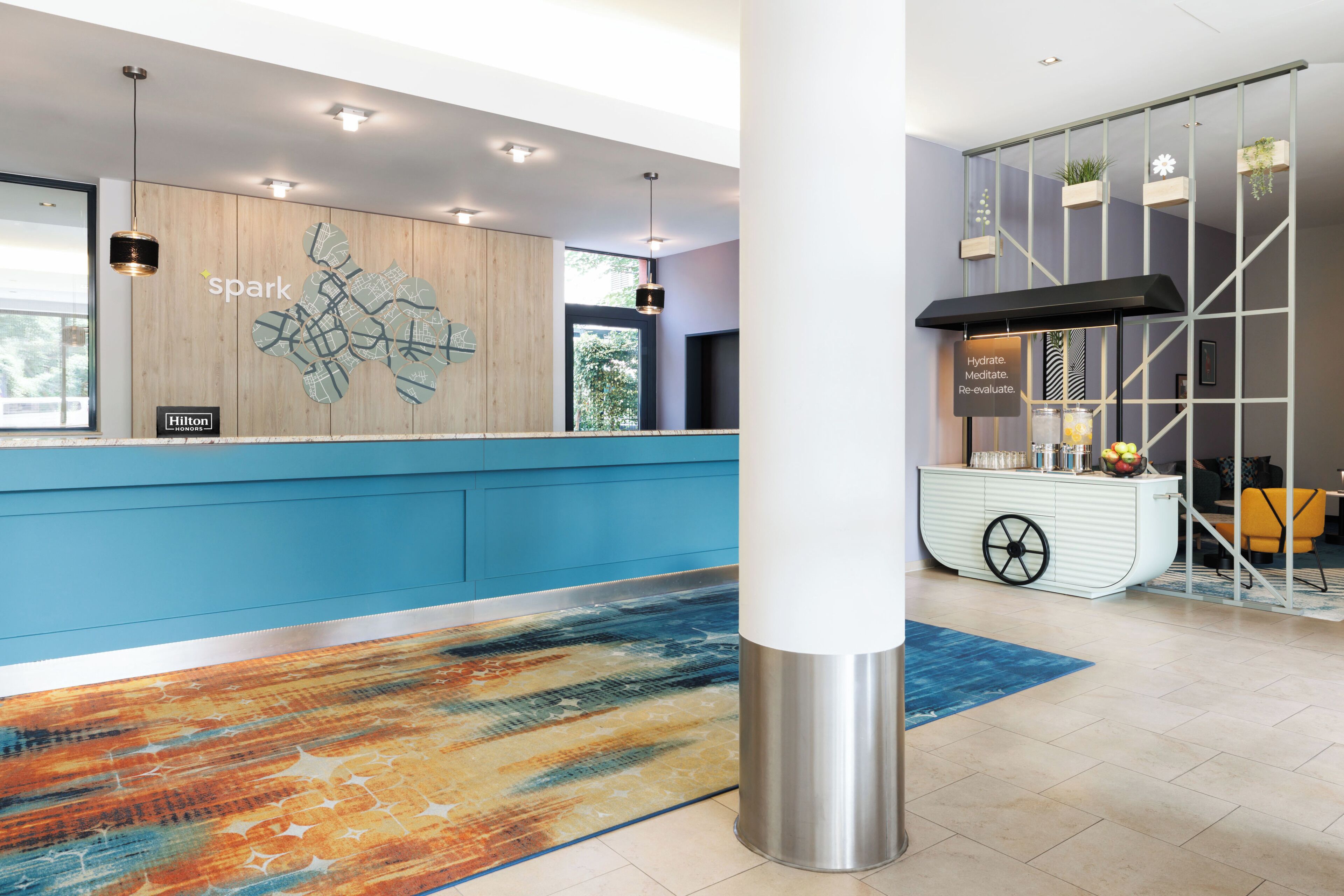 A hotel reception area with a blue counter, a map artwork, and a hydration station.