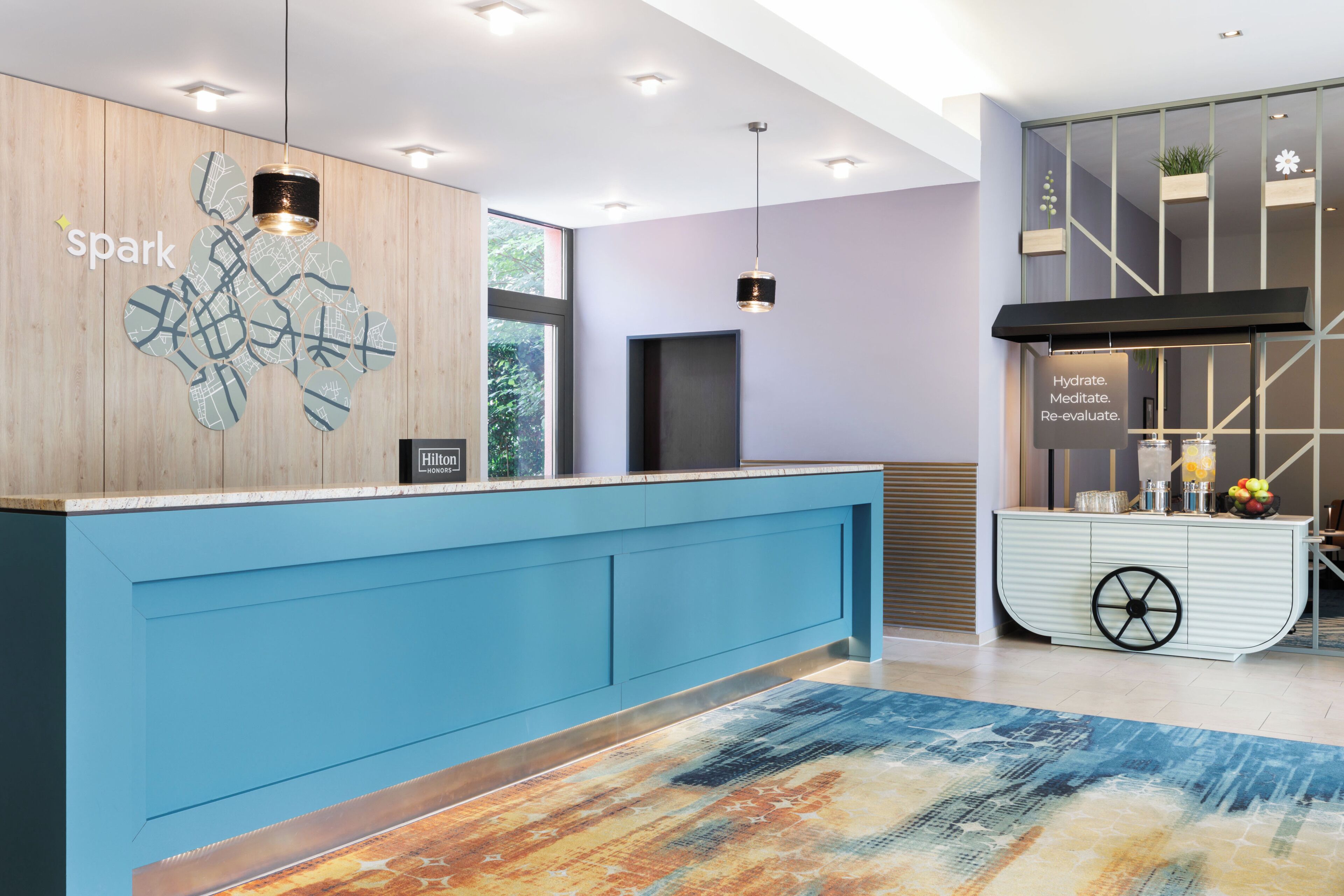 Ein Hotelrezeptionsbereich mit einem blauen Empfangstresen, einer Wanddekoration als Karte und einem an der Wand befestigten Schild.