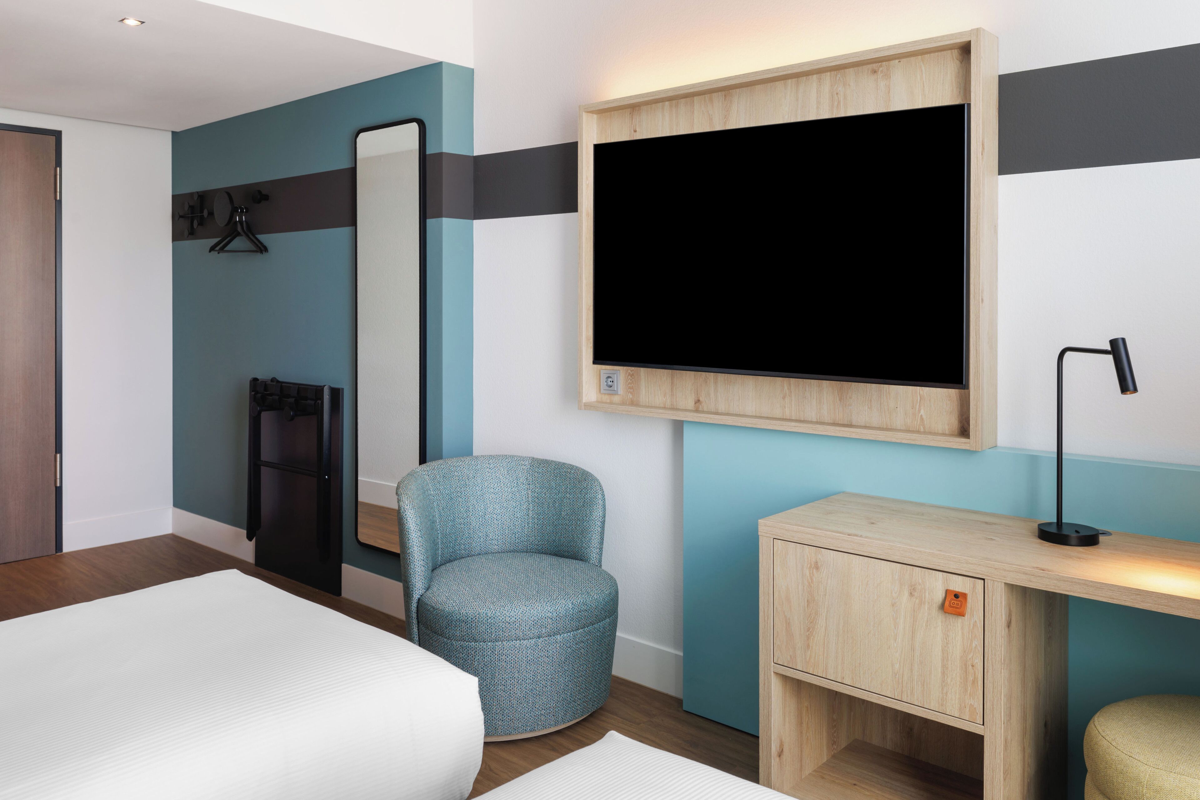 Ein Hotelzimmer mit Bett, Schreibtisch, Stuhl, Spiegel und Fernseher.