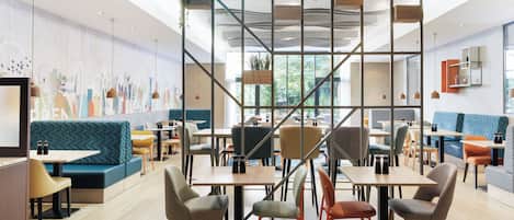 A modern cafe with wooden tables, cushioned seating, and a cityscape mural on the wall.