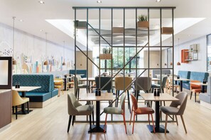 Un café moderne avec des tables en bois, des sièges confortables et une fresque représentant un paysage urbain sur le mur.