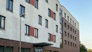Een modern gebouw met een 'spark'-bord, een parkeerplaats en een heldere lucht.