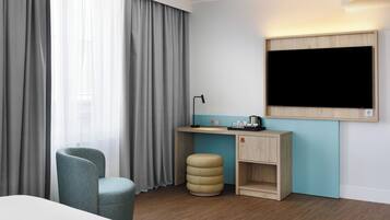 Ein Hotelzimmer mit einem Bett, einem Schreibtisch mit Lampe, einem Stuhl, einem kleinen Hocker und einem an der Wand befestigten Fernseher.