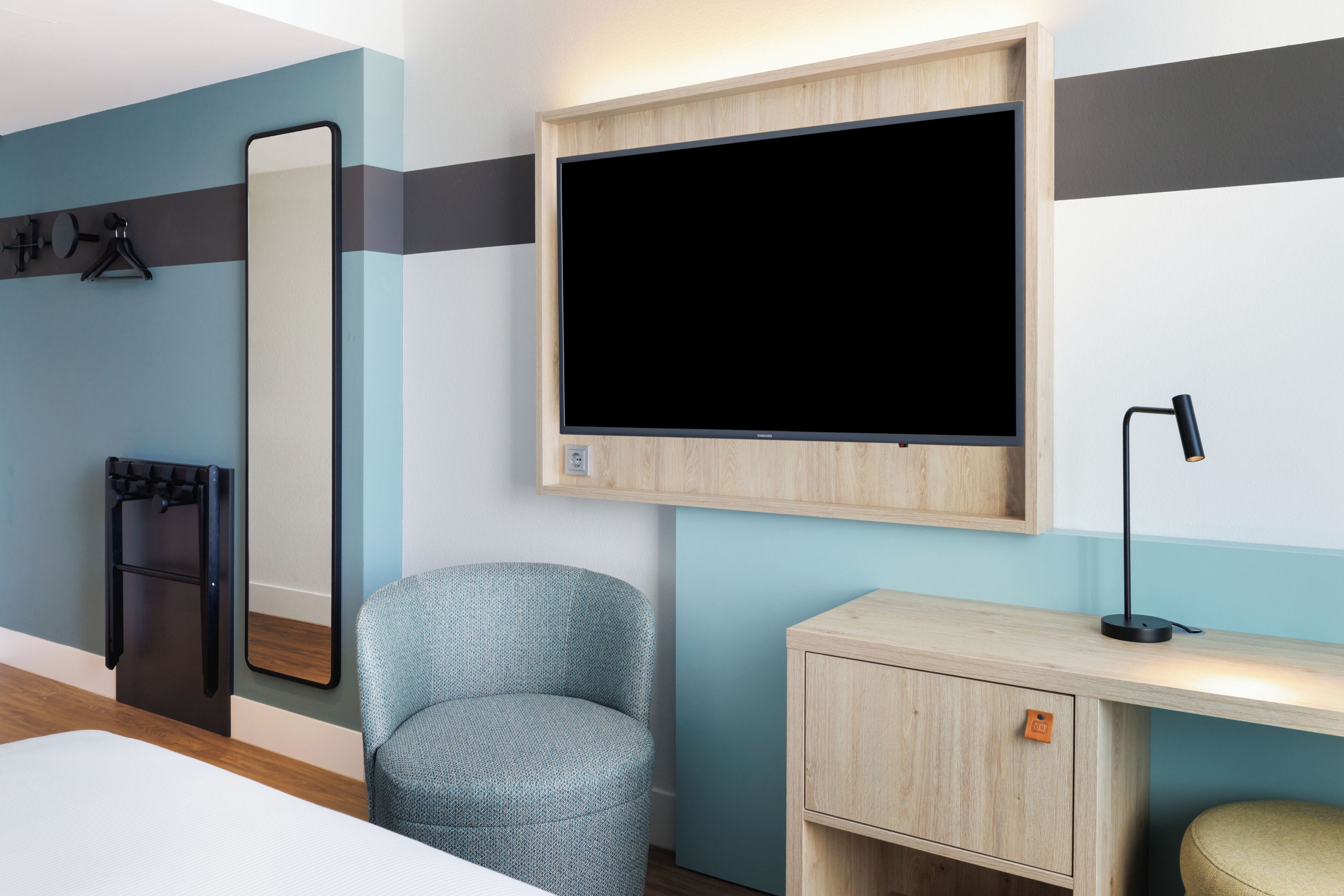 Une chambre d’hôtel comprenant un lit, un bureau avec une lampe, une chaise, un miroir et un téléviseur.
